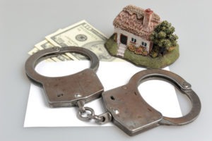 handcuffs on envelope with money next to ceramic house