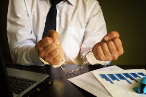 man sitting by laptop and business paperwork in cuffs